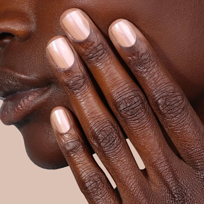 A close-up of a person's face and hand with neatly manicured, light pink nails—painted with LONDONTOWN's Bare Illuminating Nail Concealer—resting against their cheek.