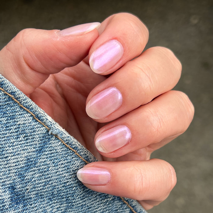Hand with short natural nails coated in Baroque gel polish showing pearly iridescent glow against denim fabric background
