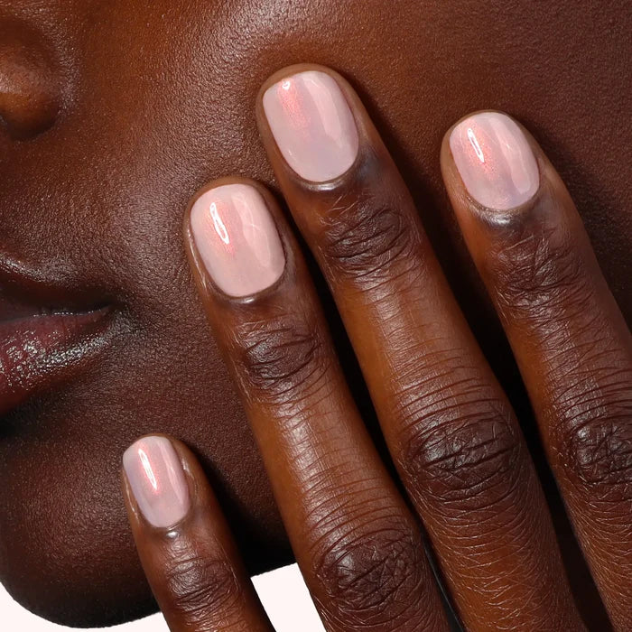 A hand with neatly manicured, bubblegum pink nails rests against a cheek, highlighting the flawless finish of LONDONTOWN Bubble Illuminating Nail Concealer.
