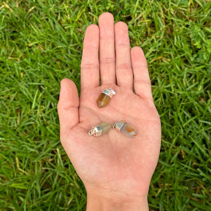 Four small raw crystal points with silver caps resting on an open hand, photographed outdoors against a background of green grass.