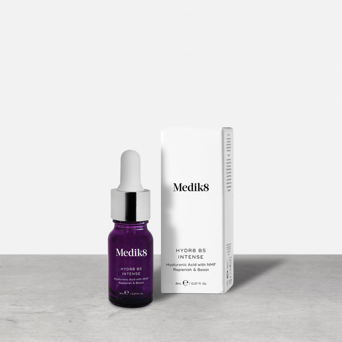 A purple 8ml glass dropper bottle of Medik8 HYDR8 B5 INTENSE serum stands next to its white packaging box on a grey surface against a white background. Text on both reads: "Medik8, HYDR8 B5 INTENSE, Hyaluronic Acid with NMF Replenish & Boost, 8mLe / 0.27 Fl. Oz.".