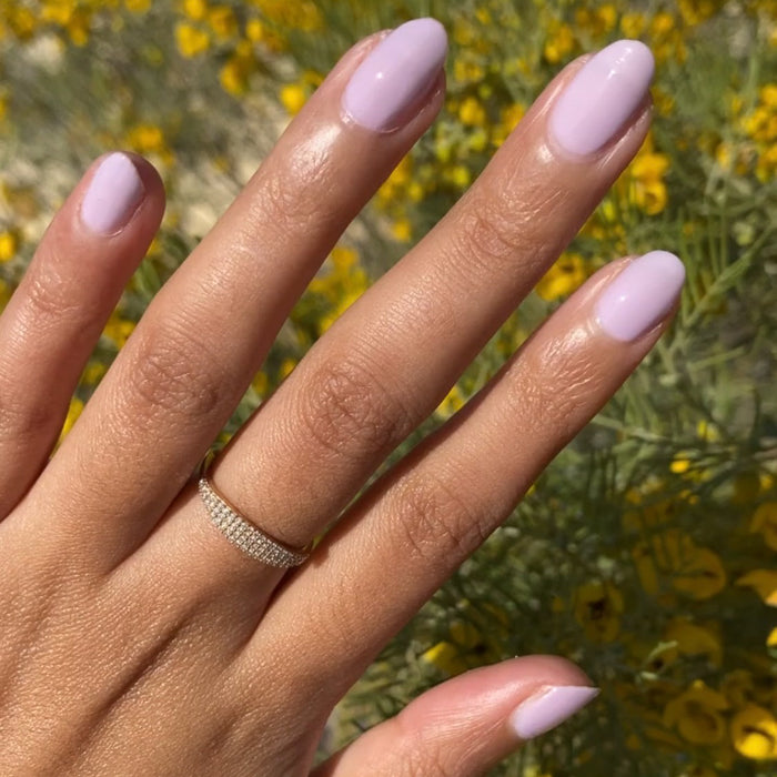 Hand with medium-length nails painted glossy Lavender Stems gel polish by Olive and June outdoors on a sunny day