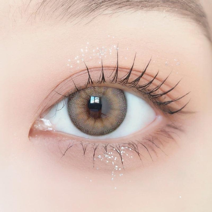 Close-up of model's eye wearing with Ann365 Buttercup Beige Korean color contact lens with prescription, complemented with barely there eye makeup, showing the brightening and enlarging effect of the circle lens on dark brown eyes.