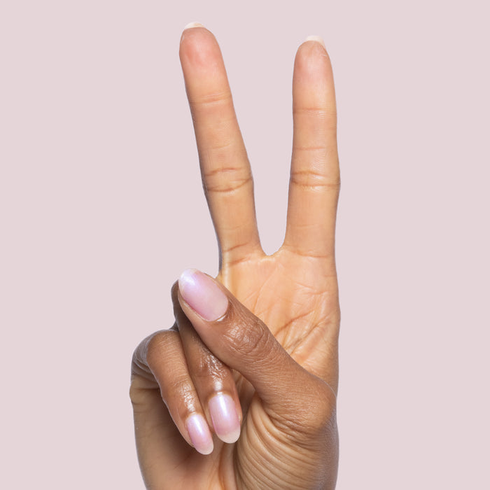 Hand with natural nails painted in Baroque gel polish showing pearly iridescent finish on light pink background