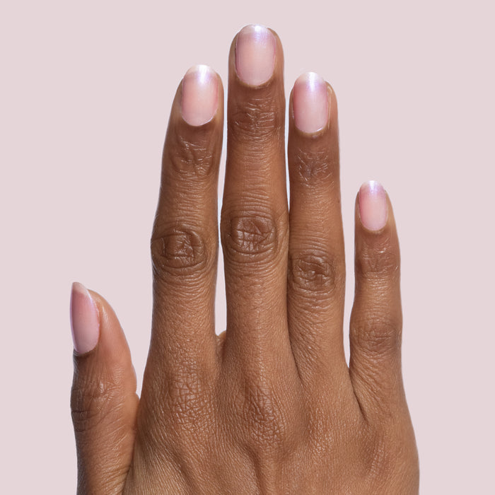 Hand with natural nails coated in Baroque gel polish showing pearly iridescent shimmer on pale pink background