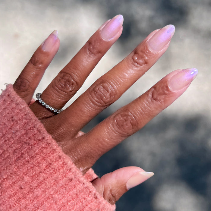 Hand with long almond-shaped nails painted in Baroque gel polish showing subtle pearly iridescent manicure outdoors
