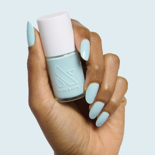 Hand with almond-shaped nails painted soft turquoise in Berry Basket polish by Olive and June holding polish bottle