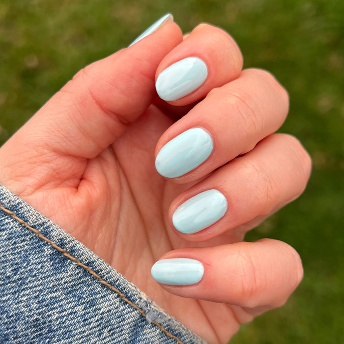 Hand with short rounded nails painted pastel turquoise in Berry Basket gel polish by Olive and June outdoors