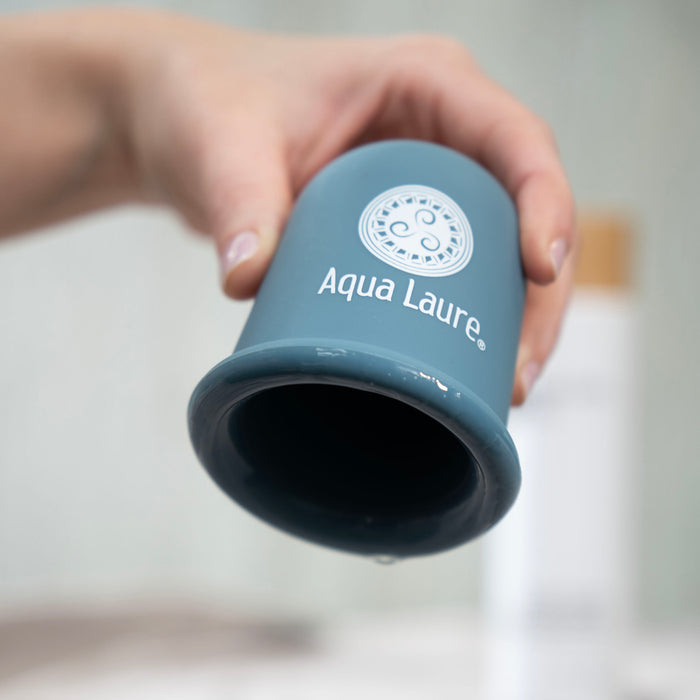Hand holding Aqua Laure® blue silicone facial cup for skin care massage and lymphatic drainage, shown with water droplets