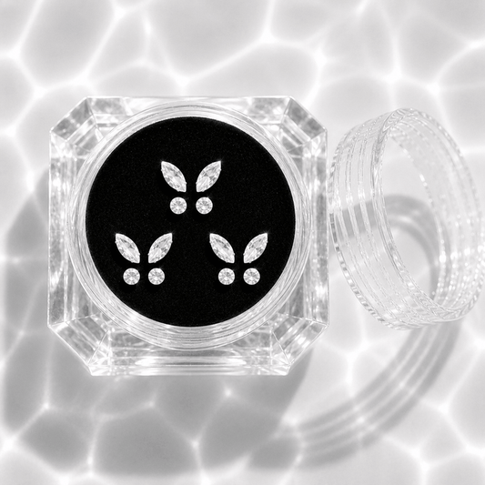 Three sets of clear crystal butterfly tooth gems in a transparent acrylic display case