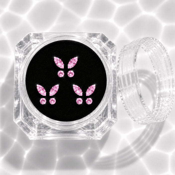 Three sets of pink crystal butterfly tooth gems in a transparent acrylic display case