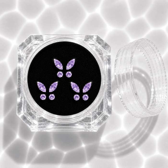 Three sets of purple crystal butterfly tooth gems in a transparent acrylic display case
