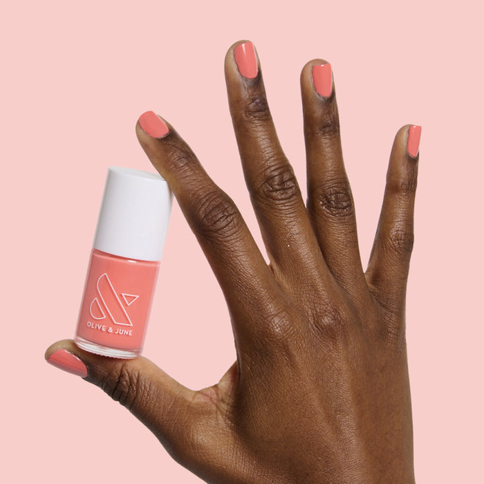 Hand with smooth nails painted in carrot orange gel polish holding Carrot Juice nail polish bottle by Olive and June