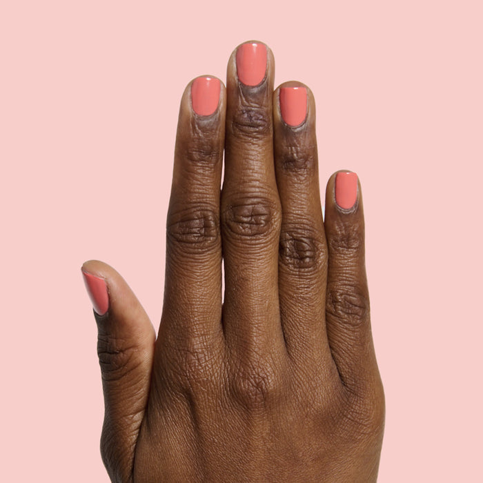 Hand with neatly trimmed nails painted bright coral orange in Carrot Juice gel polish by Olive and June
