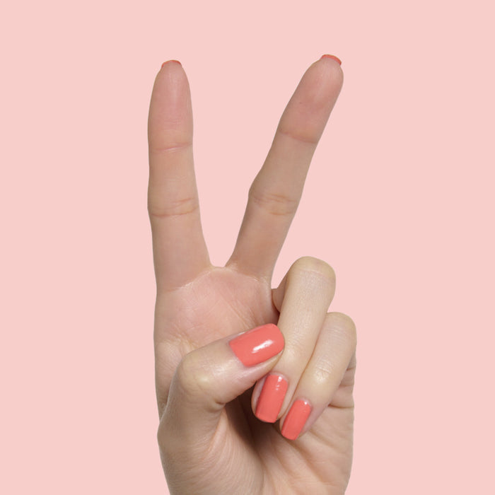 Hand displaying two fingers painted with glossy Carrot Juice gel polish by Olive and June on a pink background