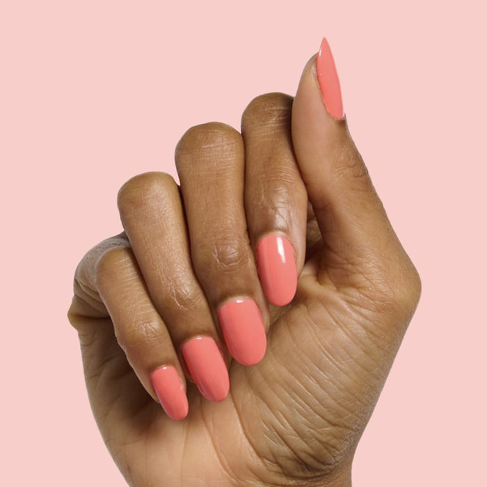 Hand with almond-shaped nails painted glossy coral shade in Carrot Juice gel polish by Olive and June