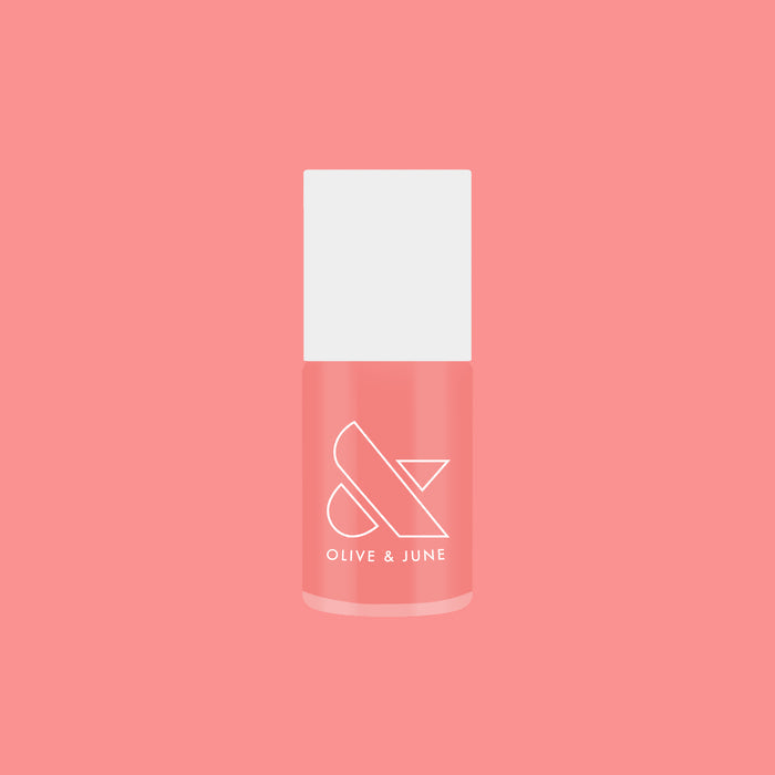 Bottle of Carrot Juice gel polish by Olive and June in a vibrant carrot orange shade on coral background