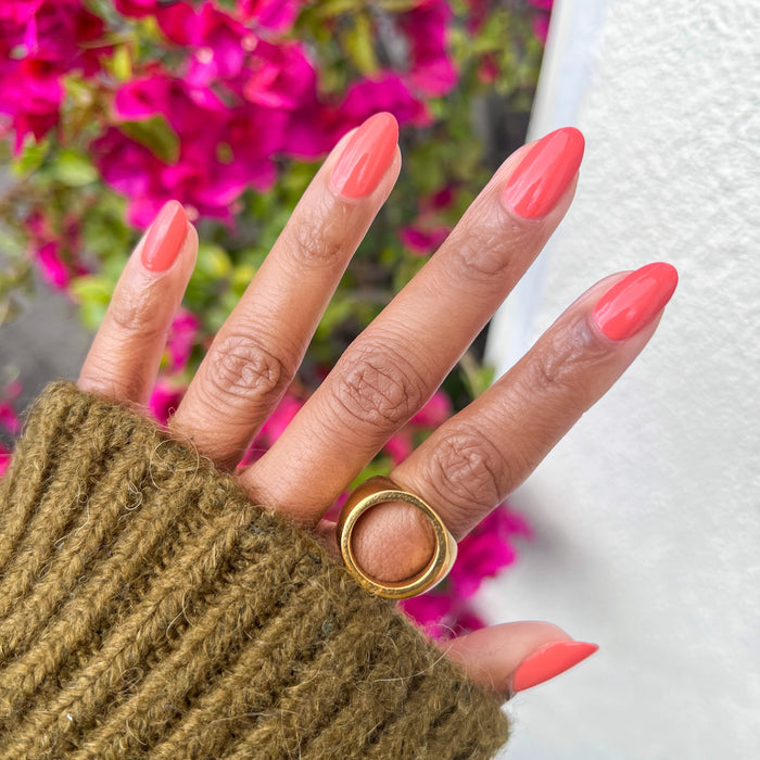 Hand with medium almond-shaped nails painted vibrant coral in Carrot Juice gel polish by Olive and June outdoors