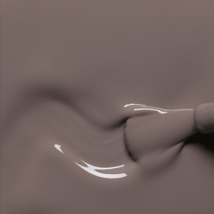 A close-up of a brush spreading glossy Clay nail polish from Manucurist, creating smooth, wavy patterns and shiny reflections on the liquid surface.