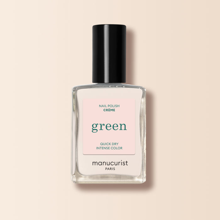 A clear glass bottle of Manucurist Crème nail polish with a black cap and light pink label rests on a beige background.