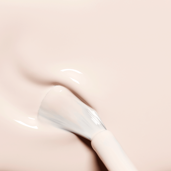 A close-up of the Manucurist Crème brush spreading a creamy pale pink and off-white polish, revealing its glossy, wet texture on a smooth surface.