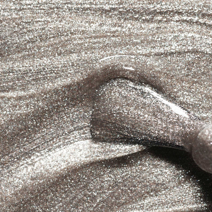 Close-up of a brush applying Manucurist's Disco polish, showcasing its opaque, glittery silver hue from the Green™ range with a sparkly, metallic texture and smooth, glossy finish.