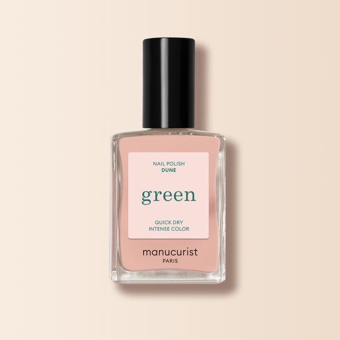 A bottle of Manucurist Dune nail polish with a black cap, labeled "green," is shown against a pale beige background. The soft nude pink shade features subtle orange undertones.