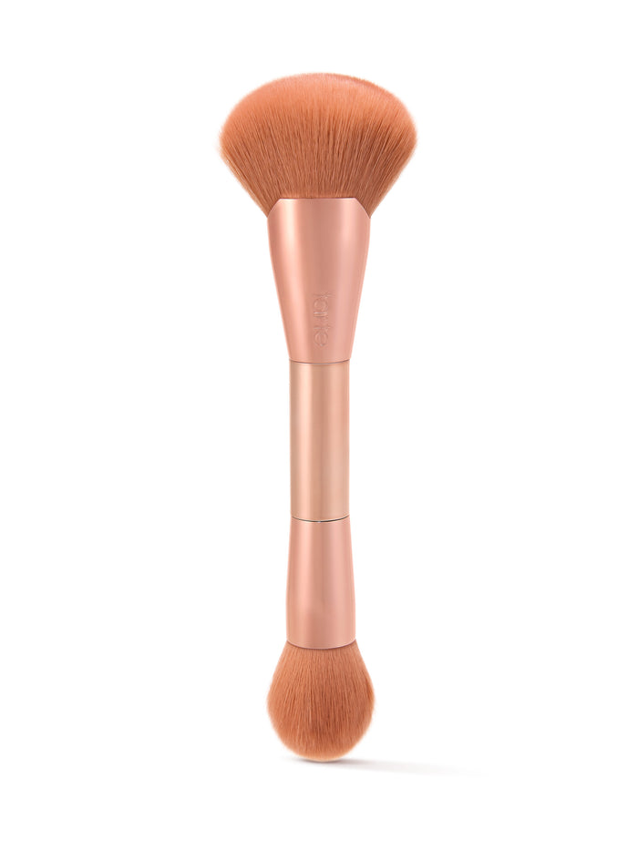 Dual-ended makeup brush with soft bristles; one end wide and fluffy, the other smaller and round. Held in a metallic handle, marked with Tarte, set against a white background.