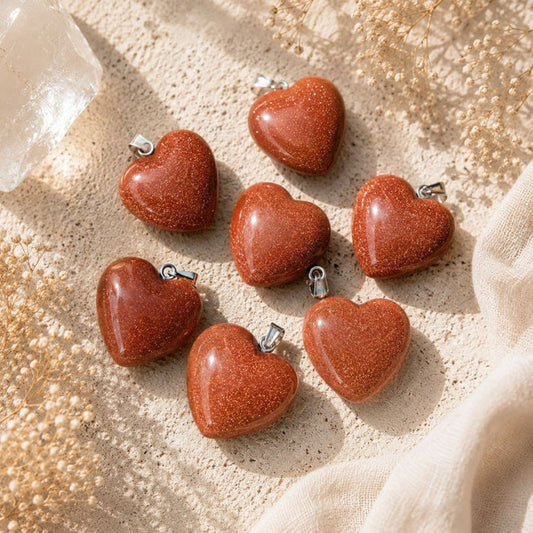 Goldstone Mini Heart Pendants with shimmering copper sparkles on a warm limestone surface with linen and dried florals.