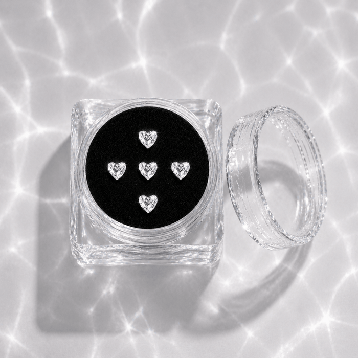 Five clear crystal heart tooth gems in a transparent acrylic display case