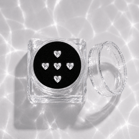 Five clear crystal heart tooth gems in a transparent acrylic display case