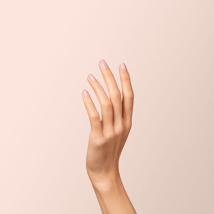 A hand with neatly manicured nails, painted in Manucurist’s sheer pink Hortencia polish, is raised against a soft beige background.