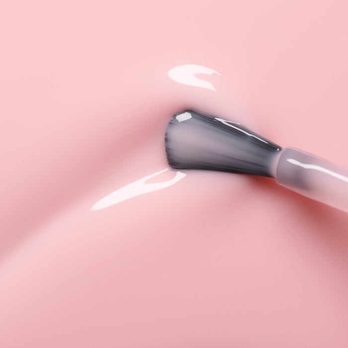 A close-up shows the Manucurist Hortencia nail polish brush applying sheer pink polish on a smooth surface, revealing a soft reflection and shine.