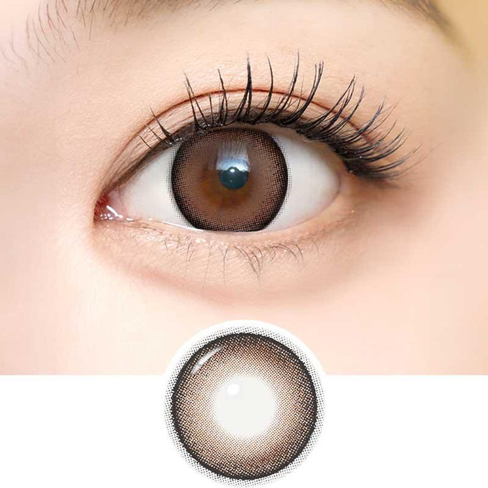 Close-up of an eye wearing i-Sha Dekame Look At Me Sand Brown contacts, showing a subtle limbal ring and long lashes. Below, an enlarged view highlights the gradient design and dekame effect of these i-Sha lenses.