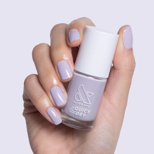 Hand holding Olive and June Jacaranda quick dry gel polish with nails painted in pastel lavender shade