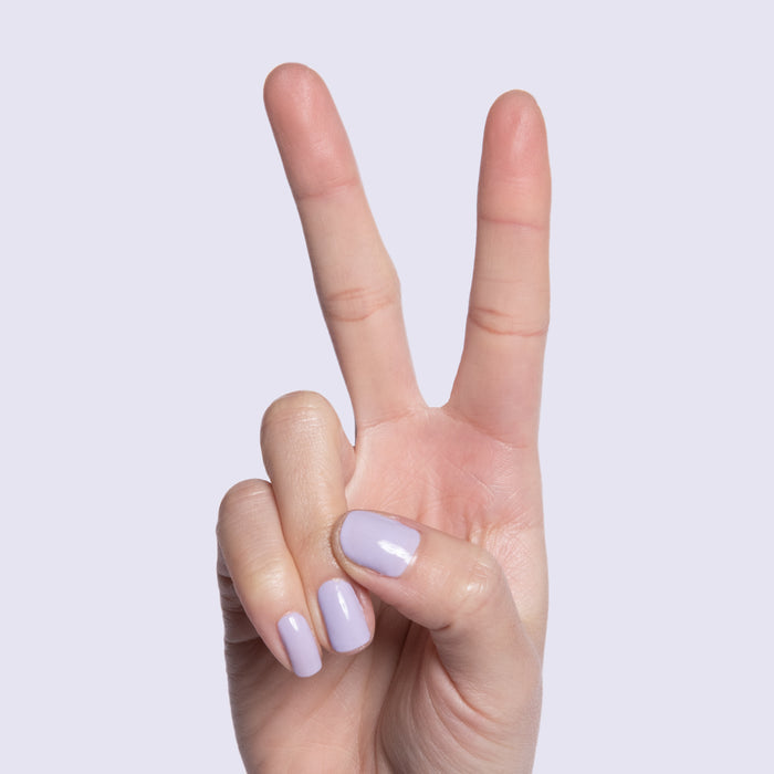 Hand showing peace sign with nails painted in pastel lavender Jacaranda quick dry gel polish on light background