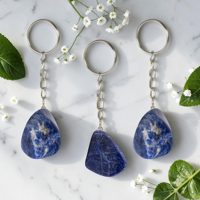 Three Sodalite keychains on a marble surface with flowers and leaves.