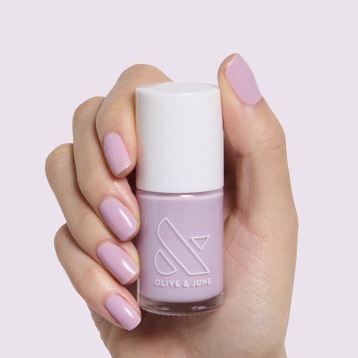 Hand holding a pale lavender nail polish bottle with nails painted in Lavender Stems by Olive and June