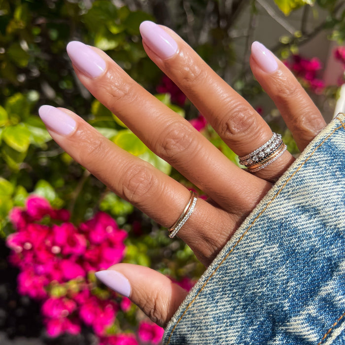 Hand with glossy nails painted soft lavender in Lavender Stems gel polish by Olive and June outdoors with flowers