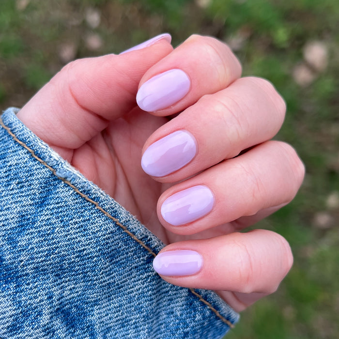 Hand with short nails painted glossy milky lavender in Lavender Stems gel polish by Olive and June outdoors