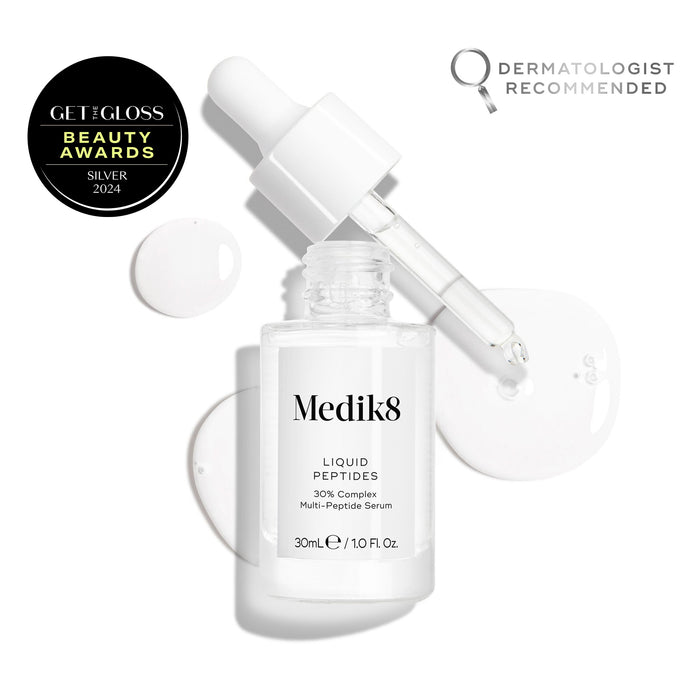 A clear glass dropper bottle of Liquid Peptides serum is presented, with its dropper removed and resting beside it and serum droplets, showing the texture.