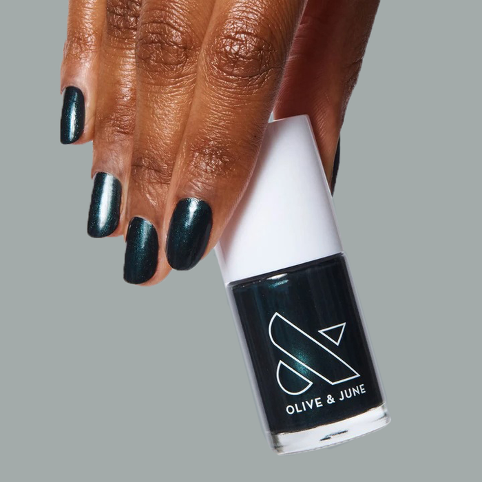 Hand with nails coated in deep shimmering emerald green LL gel polish holding Olive and June bottle for a sleek mani