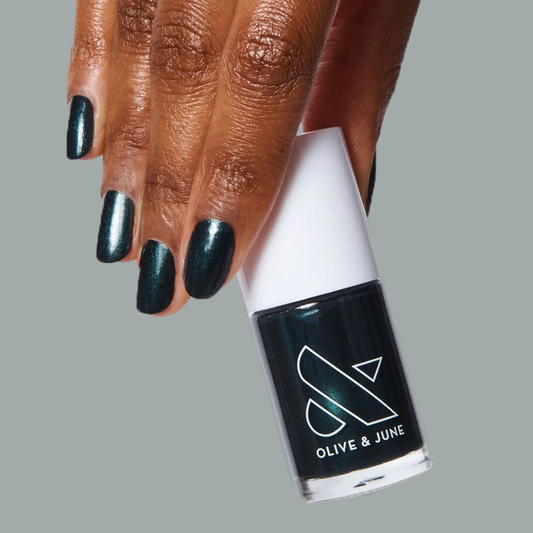 Hand with nails coated in deep shimmering emerald green LL gel polish holding Olive and June bottle for a sleek mani