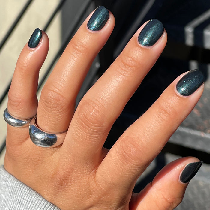 Hand with nails coated in LL gel polish in deep sparkling emerald green for a vibrant at-home manicure by Olive and June