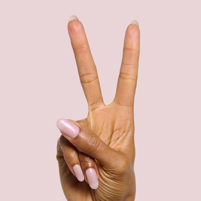 Hand showing peace sign with nails painted in soft iridescent pink Lucky Oyster long-lasting gel polish manicure
