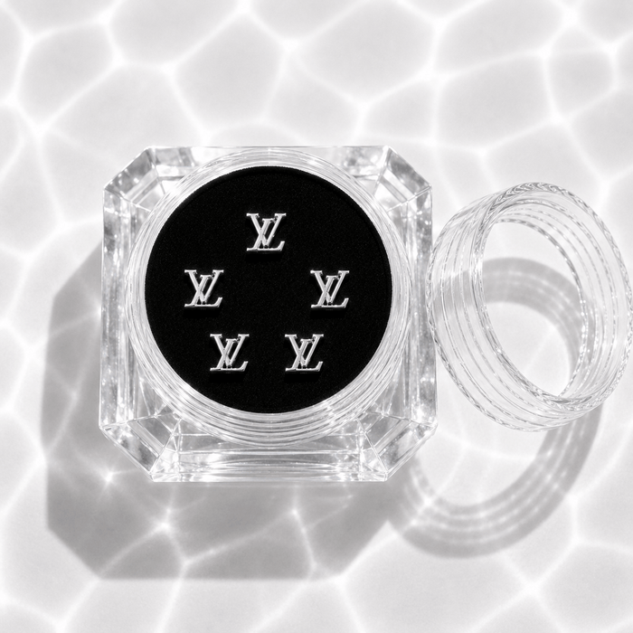 Five silver monogram tooth gem charms in a clear acrylic display case