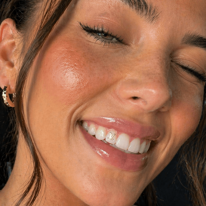 Smiling woman wearing a gold monogram tooth gem on a front tooth