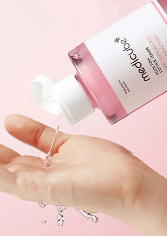 Hand holding a dropper with clear liquid next to a pink bottle labeled 'medicube' on a pink background