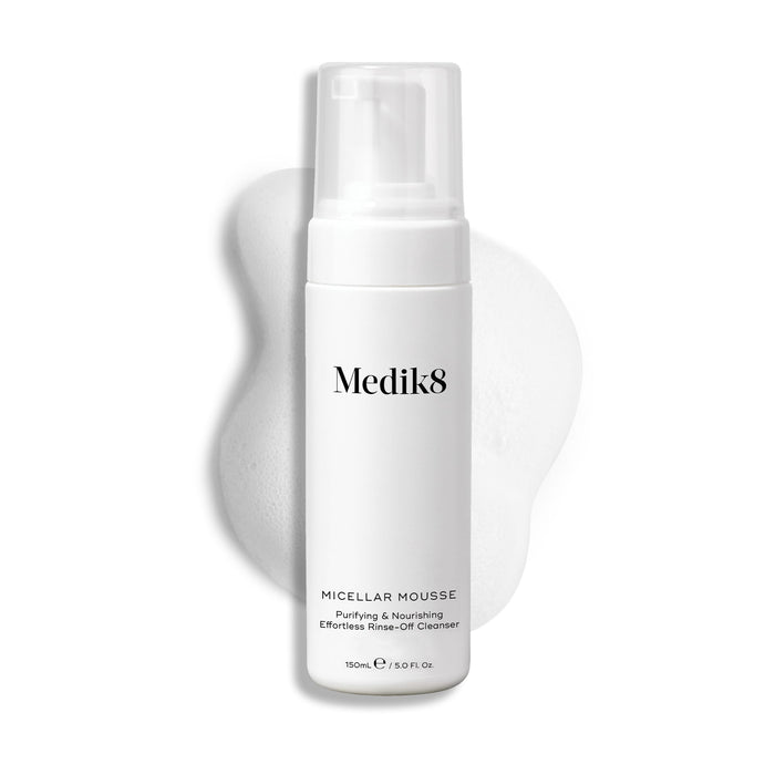 Medik8 Micellar Mousse pump bottle displayed on a white background with a smear of white foam behind it, highlighting the product's texture.