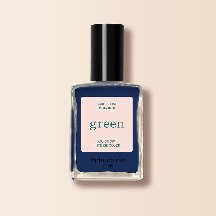 A clear bottle of Manucurist nail polish in the shade Midnight, featuring QUICK DRY INTENSE COLOR on a beige label. The midnight blue polish is visible and topped with a sleek black cap.
